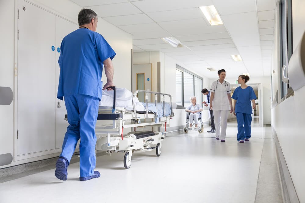 Nurse pushing a hospital bed down a hospital corridor while another doctor and nurse discuss patient care