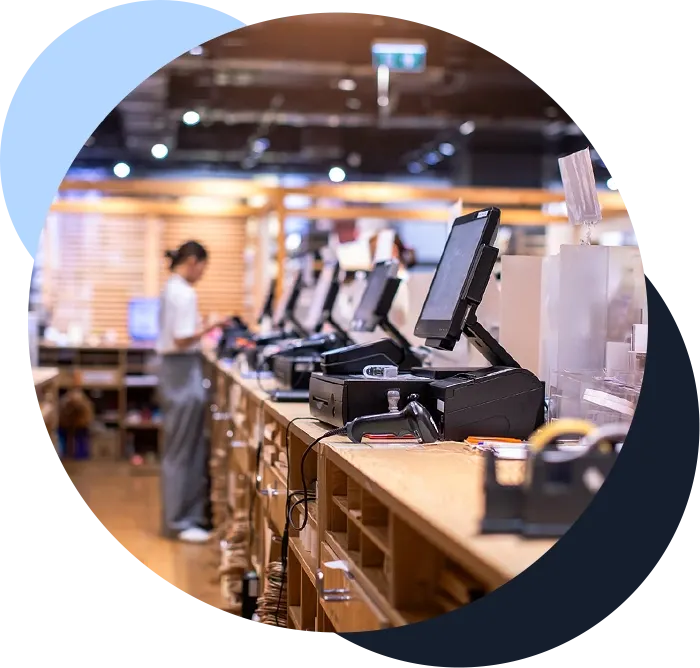Touchscreen POS terminals in a line at a retail counter with woman working at the back of the store