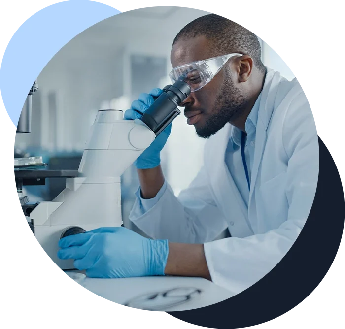 Scientist wearing safety glasses and a lab coat looking through a microscope